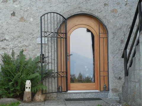 Portone ad Arco in Larice spazzolato naturale, con trattamento superficiale eseguito con vernice a basso residuo solido. Il portoncino è dotato di triplo vetrocamera con due vetri basso emissivi ed antinfortunistici con camere riempite con gas argon e distanziali a bassa conducibilità (TGI); il tutto per ottenere una vetrata termicamente efficente. Ug = 0.6